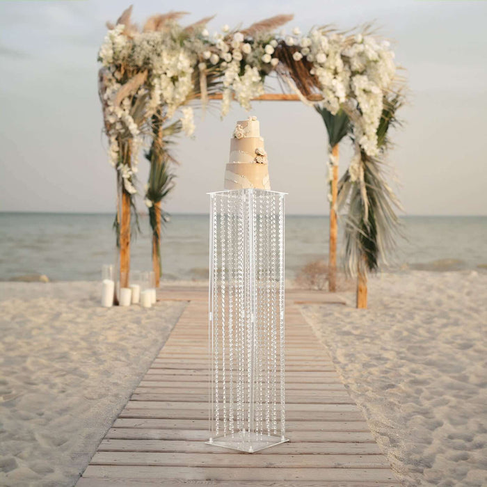 Elegant clear acrylic cake stand with cascading beads at a beach wedding altar.