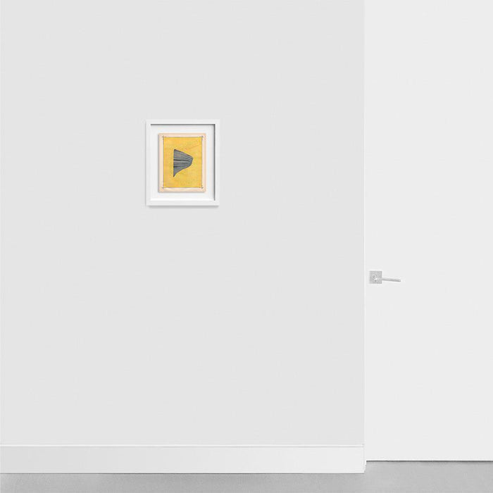 A small framed abstract print with a grey folded fabric shape on a textured yellow background hanging on a light grey
