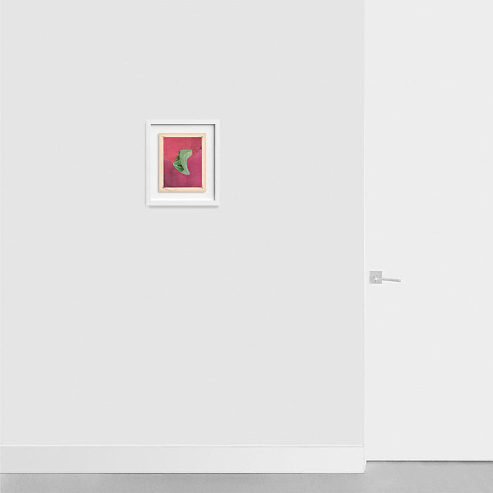Small abstract print with a green curved shape on a pink background framed in white hanging on a gray wall