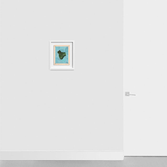 Small framed abstract print with a dark green folded shape on a blue background hanging on a light gray wall