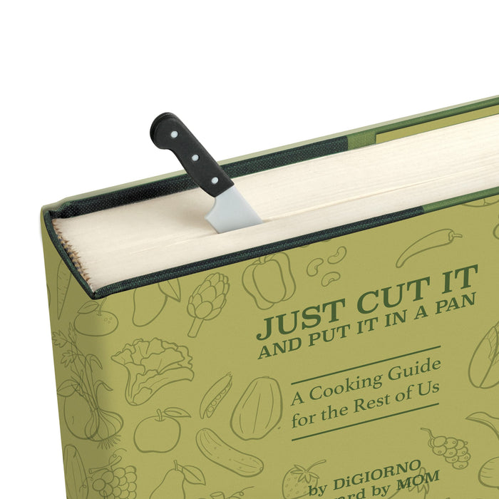A close-up of a hardcover cooking guide book titled "JUST CUT IT AND PUT IT IN A PAN" with a small kitchen knife bookmark  tucked under the open top edge. The cover is light olive green with subtle food illustrations and dark green text.