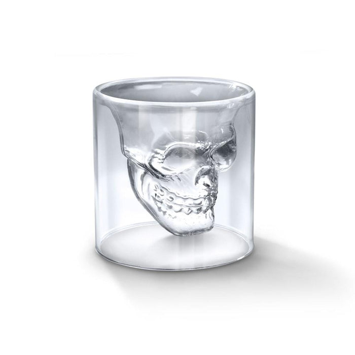 A clear crystal skull shot glass on a plain background.