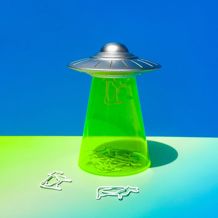 Green UFO paperclip dispenser on colorful background with cow-shaped clips — playful office or holiday gift