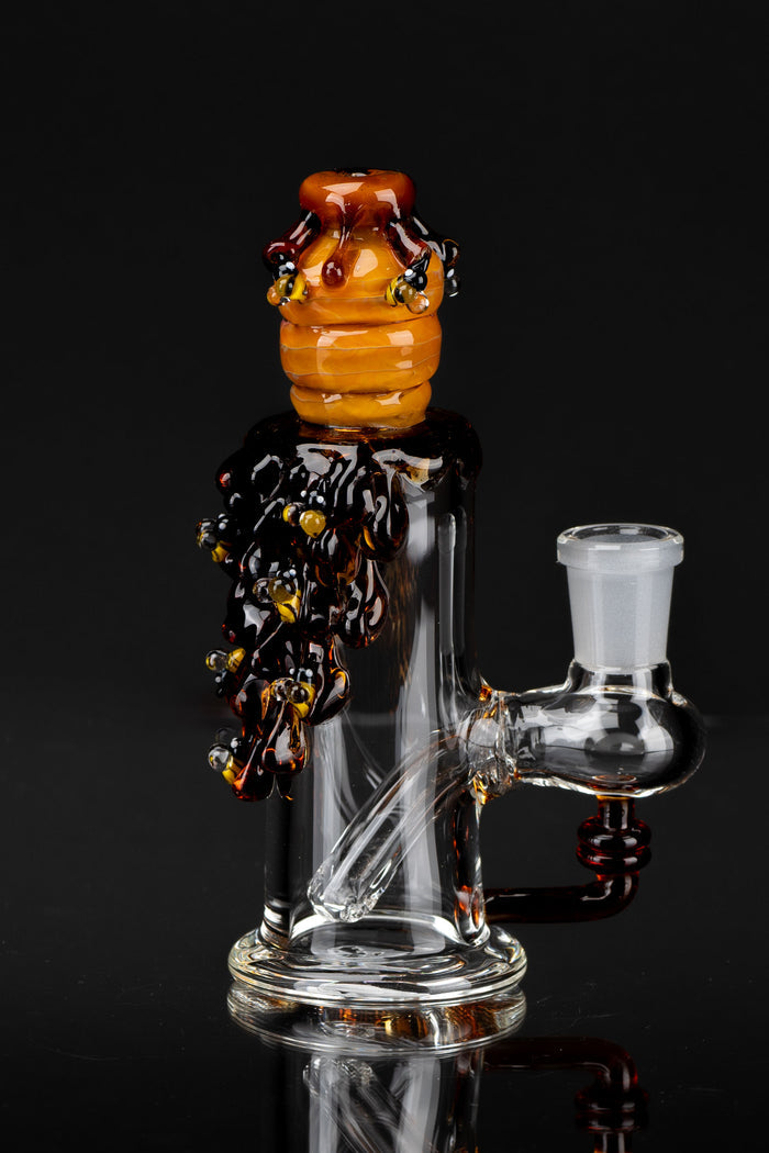 Close-up of the Mini Rig - Beehive Nano perched atop a clear glass rig, showing amber beehive detailing and dripping dark accents against a black background