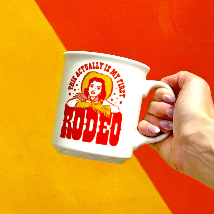 A 16oz ceramic mug that says :This actually is my first rodeo" with a cowgirl vintage illustration