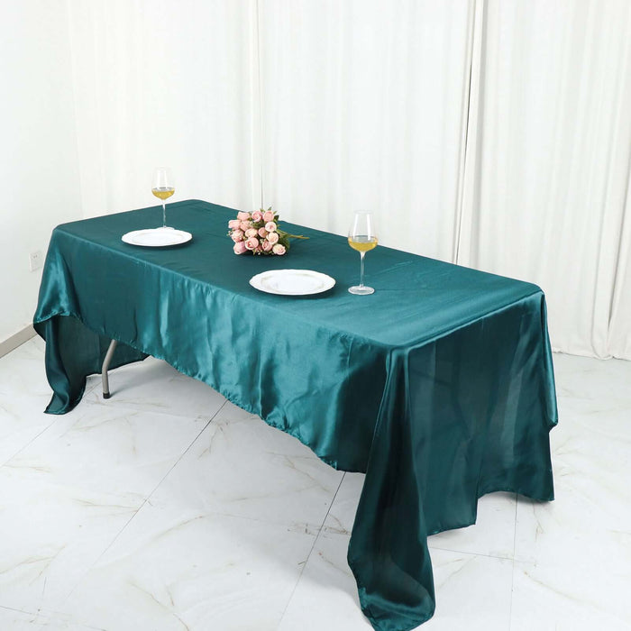 Elegant teal satin tablecloth on a dining table with plates and glasses.