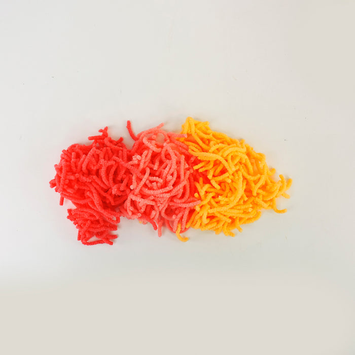 A pile of Sensory Lab Wrigglin Worms chenille stems, cut into small pieces in red, orange, and yellow, arranged together on a white background.