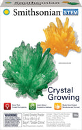 The Smithsonian Crystal Growing Value Set box displays large green and yellow crystal models, educational icons, and info on growing two crystals. This Smithsonian STEM kit offers a geology experiment for ages 10+. Warning label appears at the bottom.