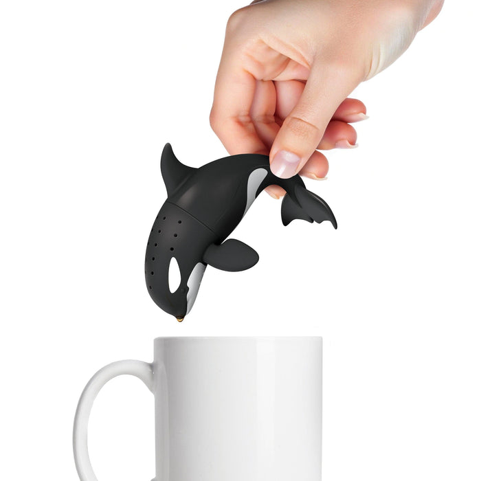 Black orca whale-shaped tea infuser being held over a white mug