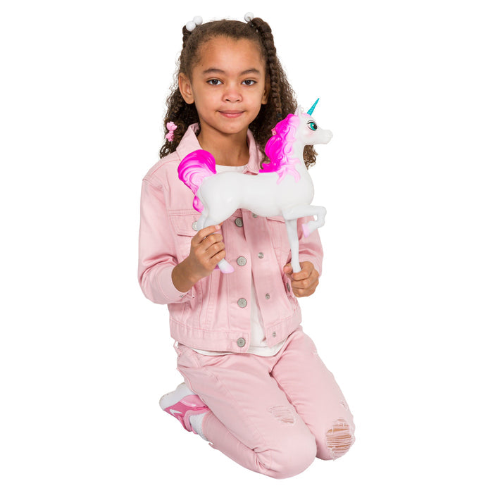 A young girl kneels and smiles while holding the Toysmith Epic Unicorn Figure, featuring a pink mane and blue horn, perfect for imaginative play. She wears a light pink jacket, matching pants, and white sneakers on a plain white background.